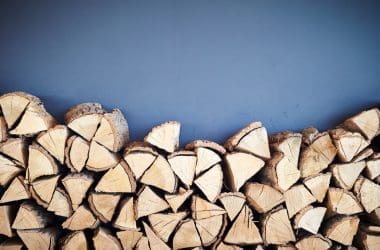 Image of a stack of firewood against a blue background for a blog post answering the question "what is a rick of firewood."