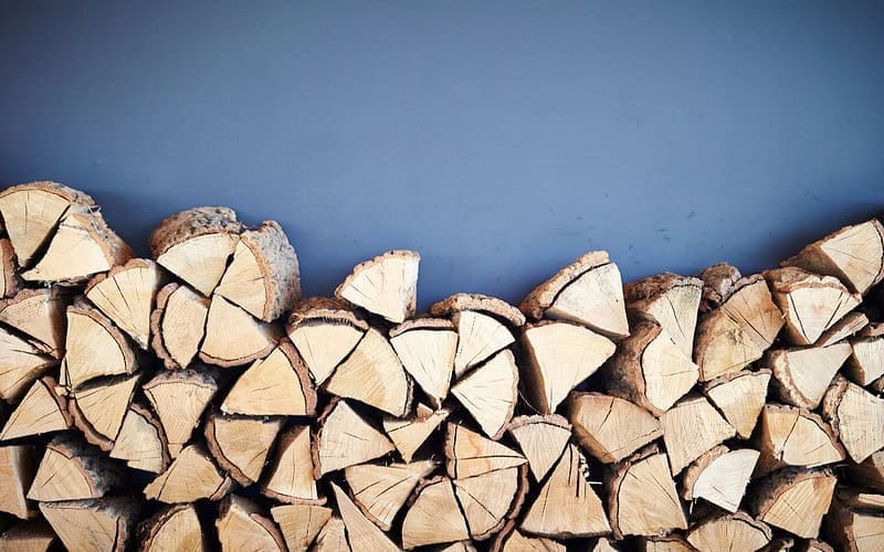Image of a stack of firewood against a blue background for a blog post answering the question "what is a rick of firewood."