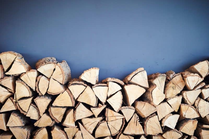 Image of a stack of firewood against a blue background for a blog post answering the question "what is a rick of firewood."