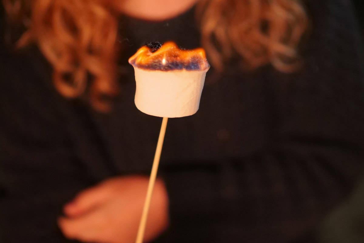 Image of a girls with a roasted marshmallow for a blog post covering roasting marshmallows over a gas fire pit.