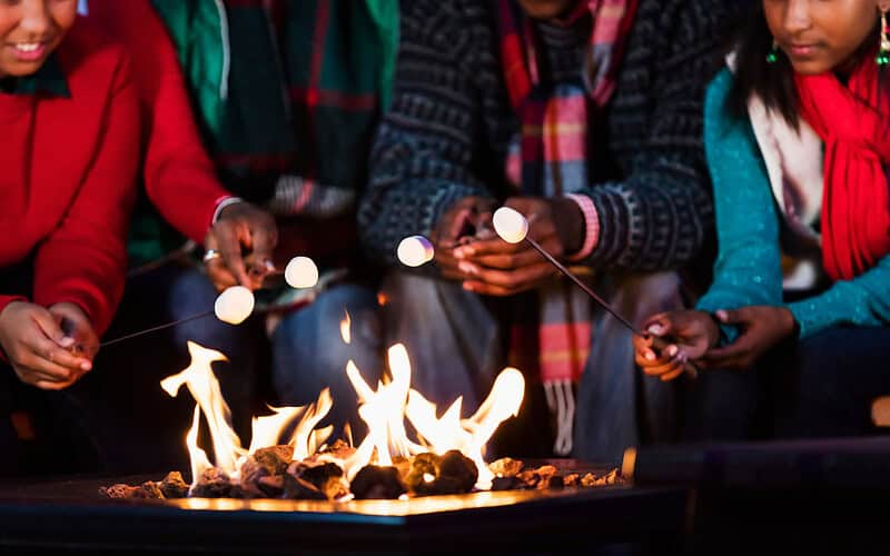 Image of a family roasting marshmallows over a gas fire pit.