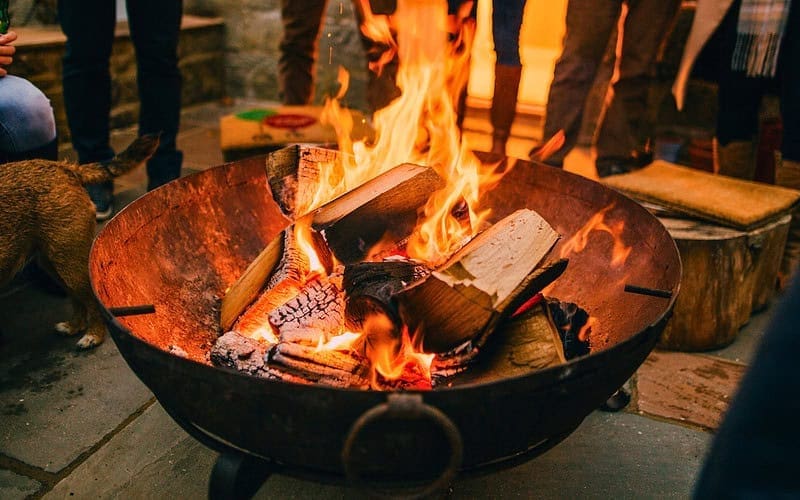Image of a large round fire pit with people around it for a blog post covering the benefits of a fire pit.