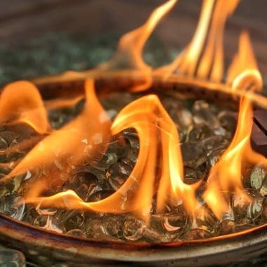 Image of a fire pit's burner ring surrounded by clear fire glass for a blog post discussing how much fire glass is needed for fire pits.