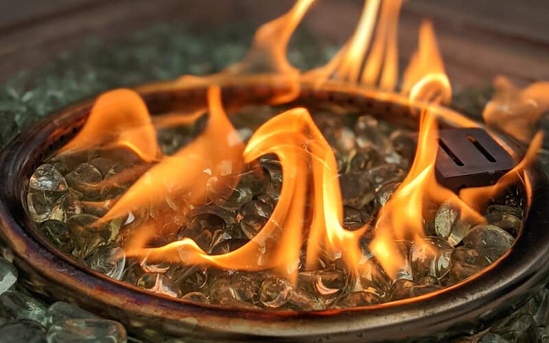 Image of a fire pit's burner ring surrounded by clear fire glass for a blog post discussing how much fire glass is needed for fire pits.