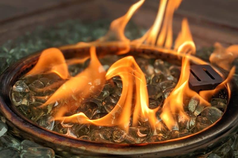 Image of a fire pit's burner ring surrounded by clear fire glass for a blog post discussing how much fire glass is needed for fire pits.