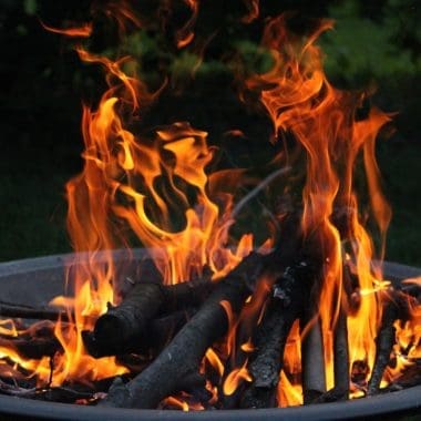 Image of a lit wood-burning fire pit early in the evening for a blog post answering the question "is a fire pit open burning?"