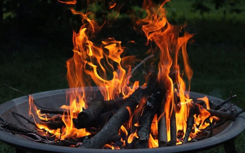 Image of a lit wood-burning fire pit early in the evening for a blog post answering the question "is a fire pit open burning?"