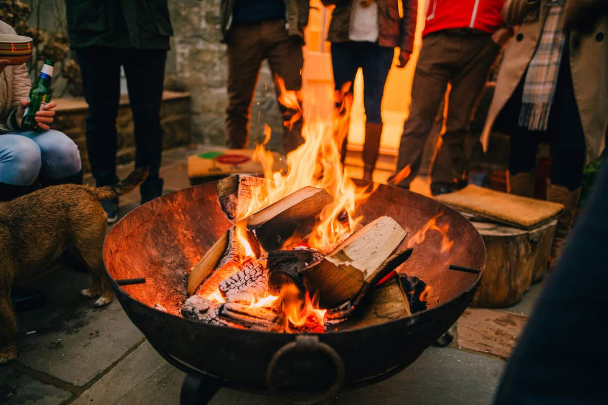 is-a-fire-pit-open-burning-main Image of a group of people around a burning fire pit for a blog post answering the question "is a fire pit open burning?"