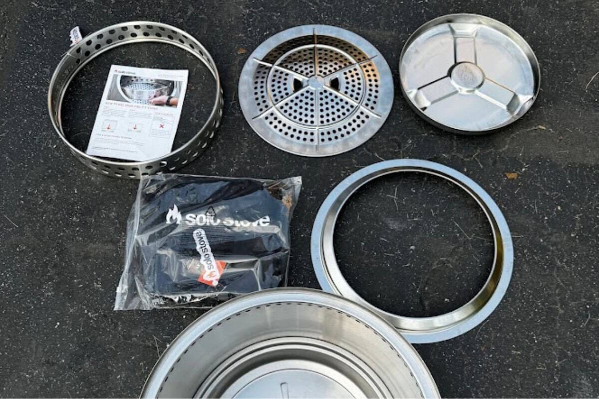 Stainless steel fire pit components including bowls, grates, and rings on a black surface, ready for assembly for backyard heating and relaxation.