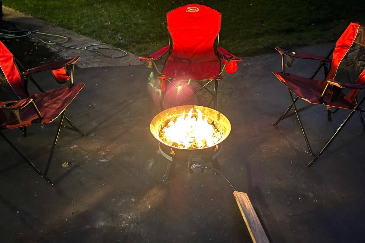 outland-living-mega-fire-pit-review-versatility Image of a gas fire pit surrounded by folding chairs at night.