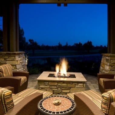 Image of an evening scene showing a glowing gas fire pit under covered patio with comfortable outdoor chairs arranged around the flames for cozy nighttime gathering.