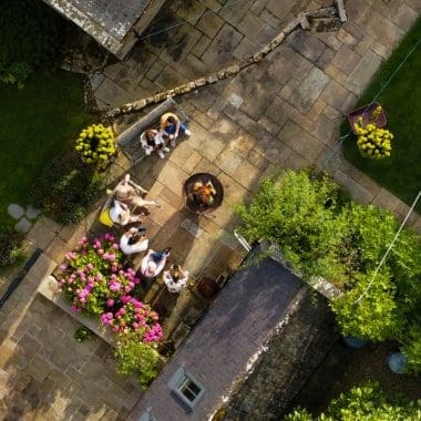 Image of a family sitting around a fire pit from above for an article discussing fire pit clearance requirements.