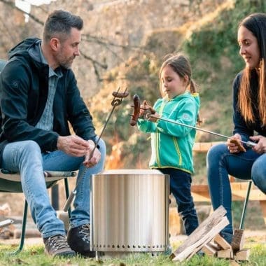 Image of a family roasting sausages over a smokeless fire pit for an article covering the best fire pit for suburban backyard use.