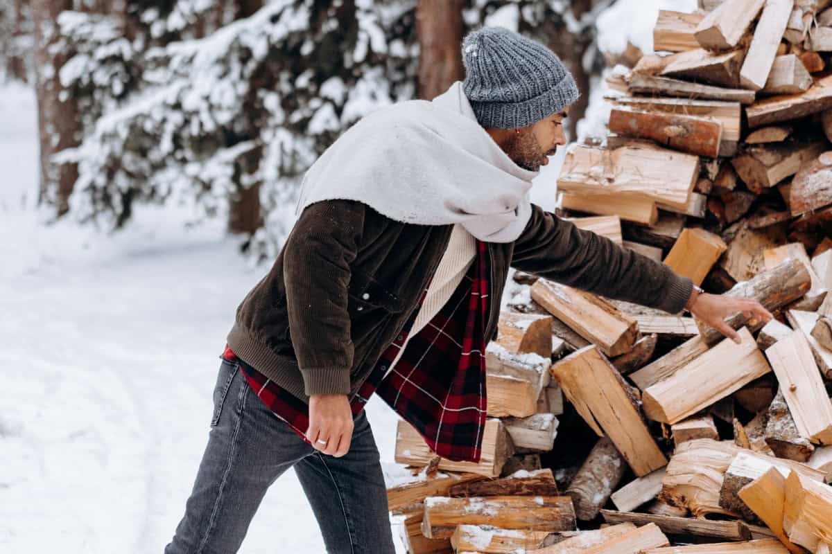 canadian-firewood-prices-seasonal demand Image of a man gathering firewood from large pike during a snowy winter day.