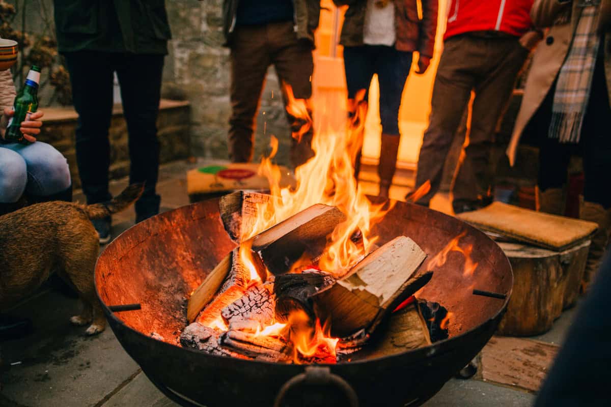 Image of a group of people standing around a burning fire pit on a cool day.