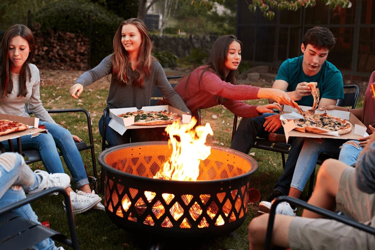 Image of a group of teenagers eating pizza around the fire pit for an article covering fire pit safety statistics.