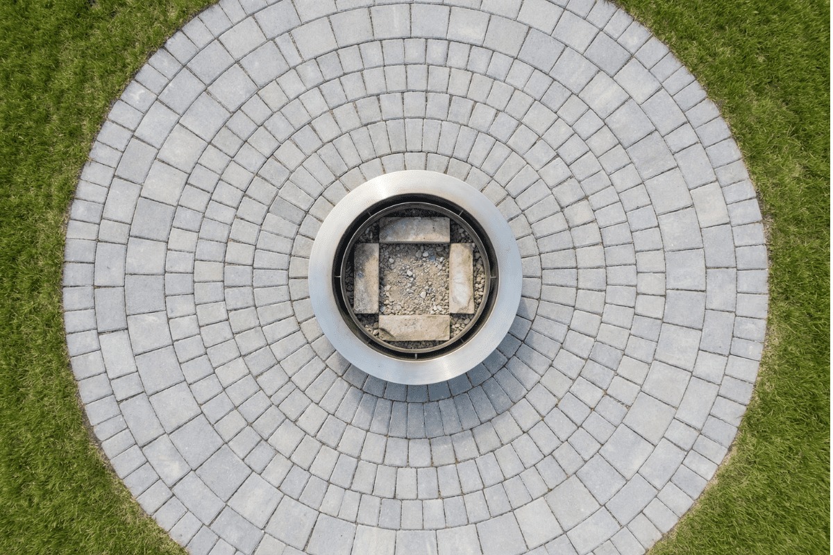 Round fire pit sitting on a properly installed paver stone base in a backyard, demonstrating a safe non-combustible surface